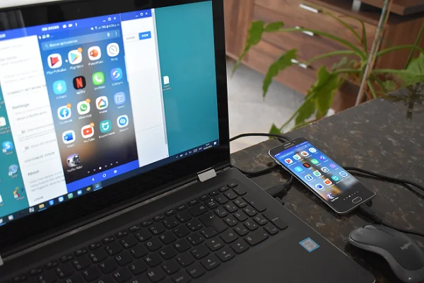 Teléfono Android conectado a una laptop mediante cable USB. La laptop muestra la pantalla del teléfono.