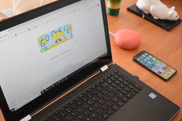 Pantalla de laptop mostrando la página de Google. También se observa un iPhone y un Google Home Mini
